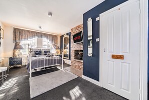 A bedroom with a bed, a television, a fireplace, and a door labeled 'En Suite.' - En-Suite Double with Parking · Walk to Whitby Abbey & 199 Steps (North Yorkshire)