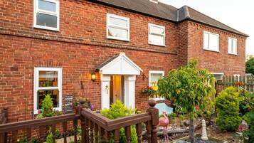 A brick house with a front porch, a small garden with a flamingo, and a wooden fence.
