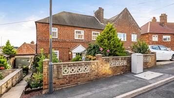 A residential brick house with a paved driveway, a garage, and a garden with various plants and flowers.