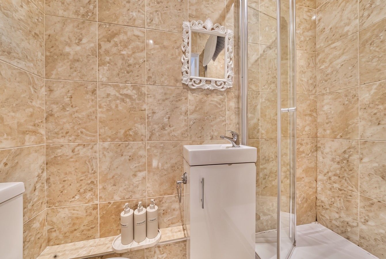 A bathroom with a glass shower enclosure, a white sink, and a marble-tiled wall.