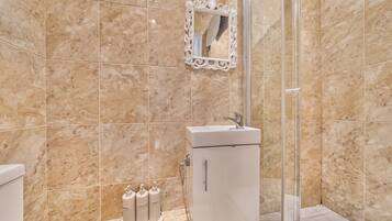 A bathroom with a glass shower enclosure, a white sink, and a marble-tiled wall.