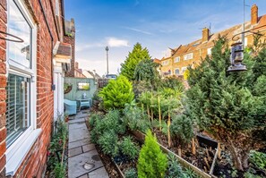 A narrow garden pathway flanked by brick houses, with a variety of potted plants and a small seating area. - En-Suite Double with Parking · Walk to Whitby Abbey & 199 Steps (North Yorkshire)