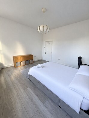 A bedroom with a large bed, a wooden bench, a door, and a hanging light fixture.