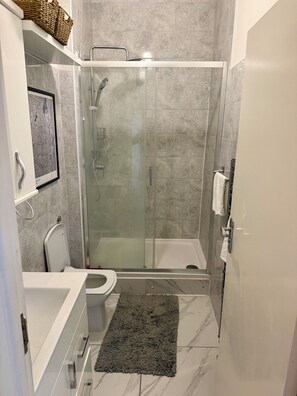 Un bany modern amb plat de dutxa de vidre, vàter i banyera.