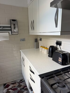 A compact kitchen with white cabinets, a gas stove, a toaster, and a kettle.