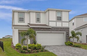 A two-story residential house with a garage, a stone accent wall, and a landscaped front yard with various plants. - 7BR house with private pool in Windsor Island (Davenport)