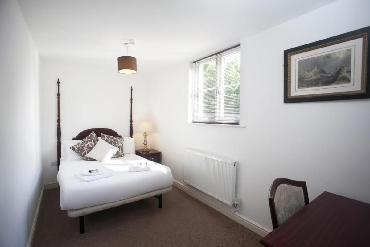 A bedroom with a bed, bedside table, lamp, window, and a framed picture on the wall.