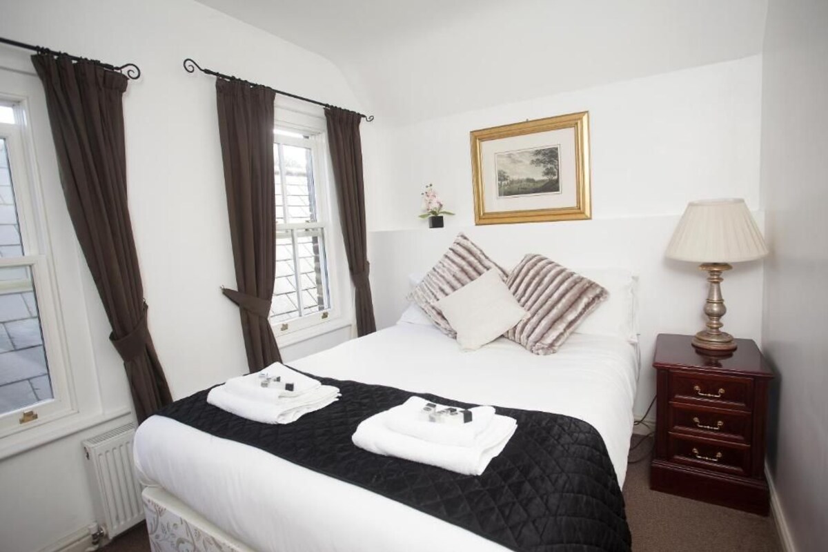 A hotel room with a bed, a nightstand, a lamp, a framed picture on the wall, and curtains on the windows.