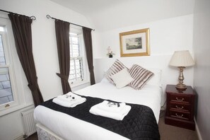A hotel room with a bed, a nightstand, a lamp, a framed picture on the wall, and curtains on the windows. - The Five Bells (Ringwould)