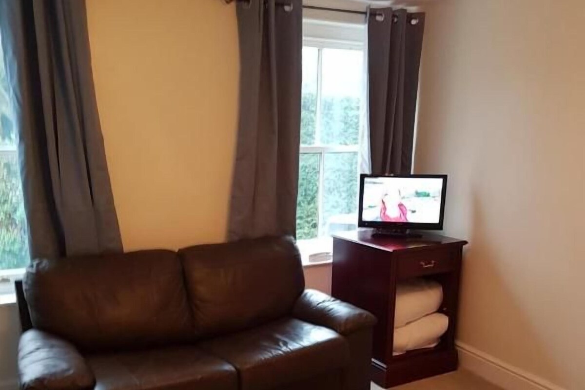 A living room with a brown leather sofa, a small wooden TV stand, and a window with curtains.