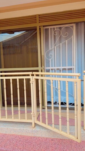 A balcony with a beige metal railing and a glass door with a decorative metal design. - C&K Homes . (Kampala)