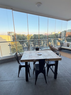 Ein geräumiger Balkon mit Esstisch und Stühlen, mit Blick auf eine Stadtlandschaft mit Gebäuden und Bäumen.