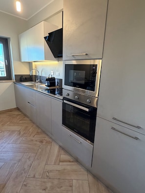 Eine moderne Küche mit Edelstahlgeräten, einem Fischgrätparkett und einem Fenster, das für natürliches Licht sorgt.