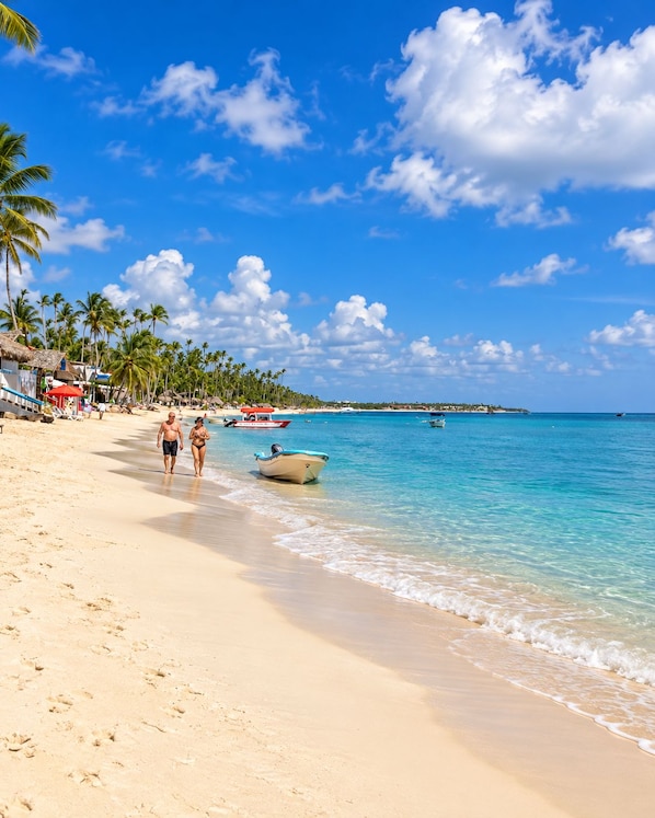 Una playa con aguas azul turquesa, palmeras y un bote en la orilla.