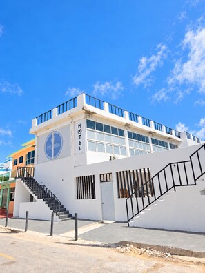 A hotel with a white facade, a blue logo, and a staircase leading to the entrance. - Hotel Canela (Punta Cana)
