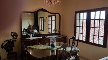A dining area with a table, chairs, a chandelier, a large mirror, and a window with a view of a tiled roof.
