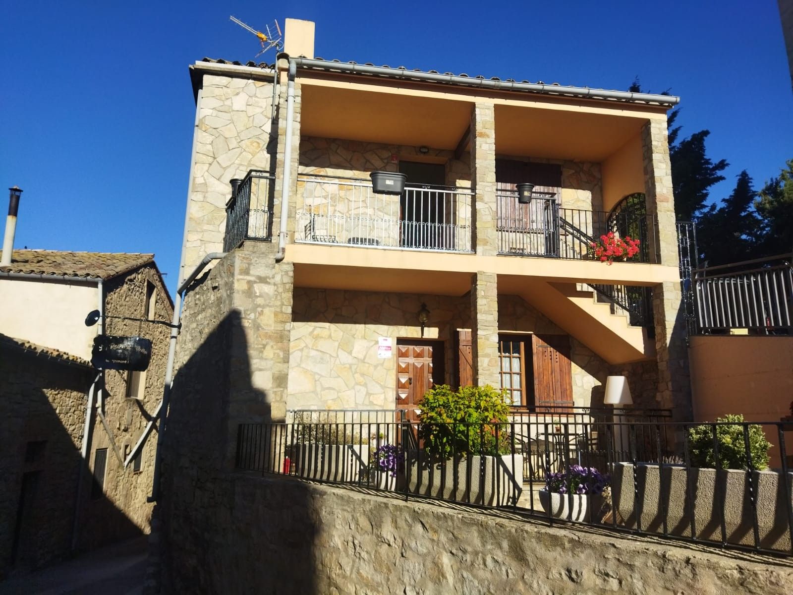 Un bâtiment à deux étages, doté de murs en pierre, de balcons avec des garde-corps en métal et d’un escalier menant à l’étage supérieur.