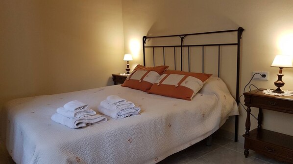 Una cama bien tendida con toallas dobladas, un cabecero de metal, lámparas de noche y una mesita de noche de madera.