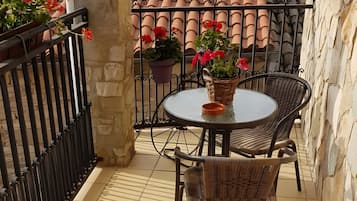 Een balkon met een ronde tafel, rieten stoelen, potplanten en een betegelde vloer.