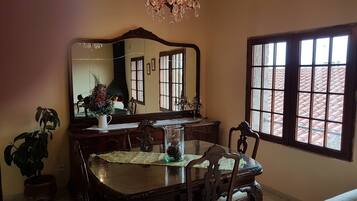 A dining area with a wooden table, chairs, a chandelier, a large mirror, and a window with a view of a tiled roof.