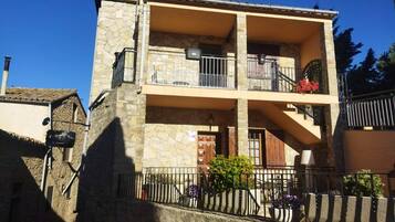 A two-story building with stone walls, balconies with metal railings, and a stone staircase leading to the upper floor.
