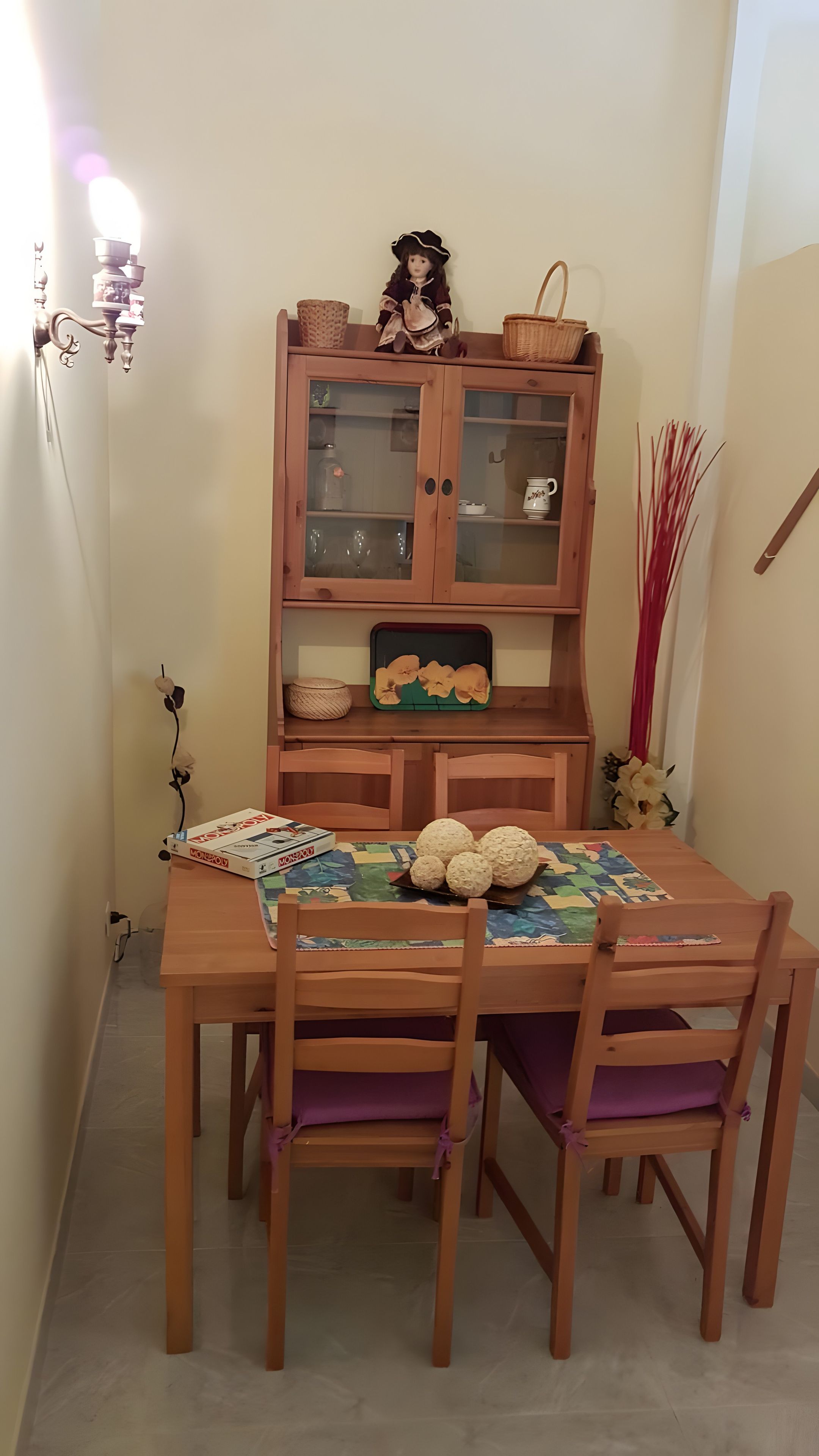 A dining table with four chairs, a wooden cabinet with glass doors, and a chandelier.