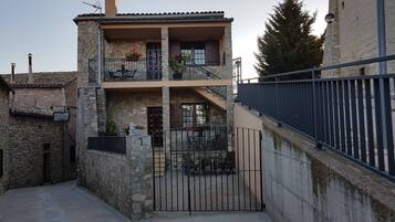 Un edificio de dos pisos con balcón, escaleras y entrada protegida por una reja.
