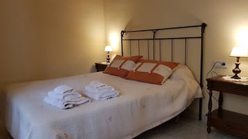 Een opgemaakt bed met opgevouwen handdoeken, een metalen hoofdbord, bedlampjes en een houten nachtkastje.