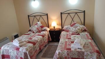 A room with two single beds, each with a floral-patterned bedspread and pillows, a nightstand with a lamp, and a radiator.