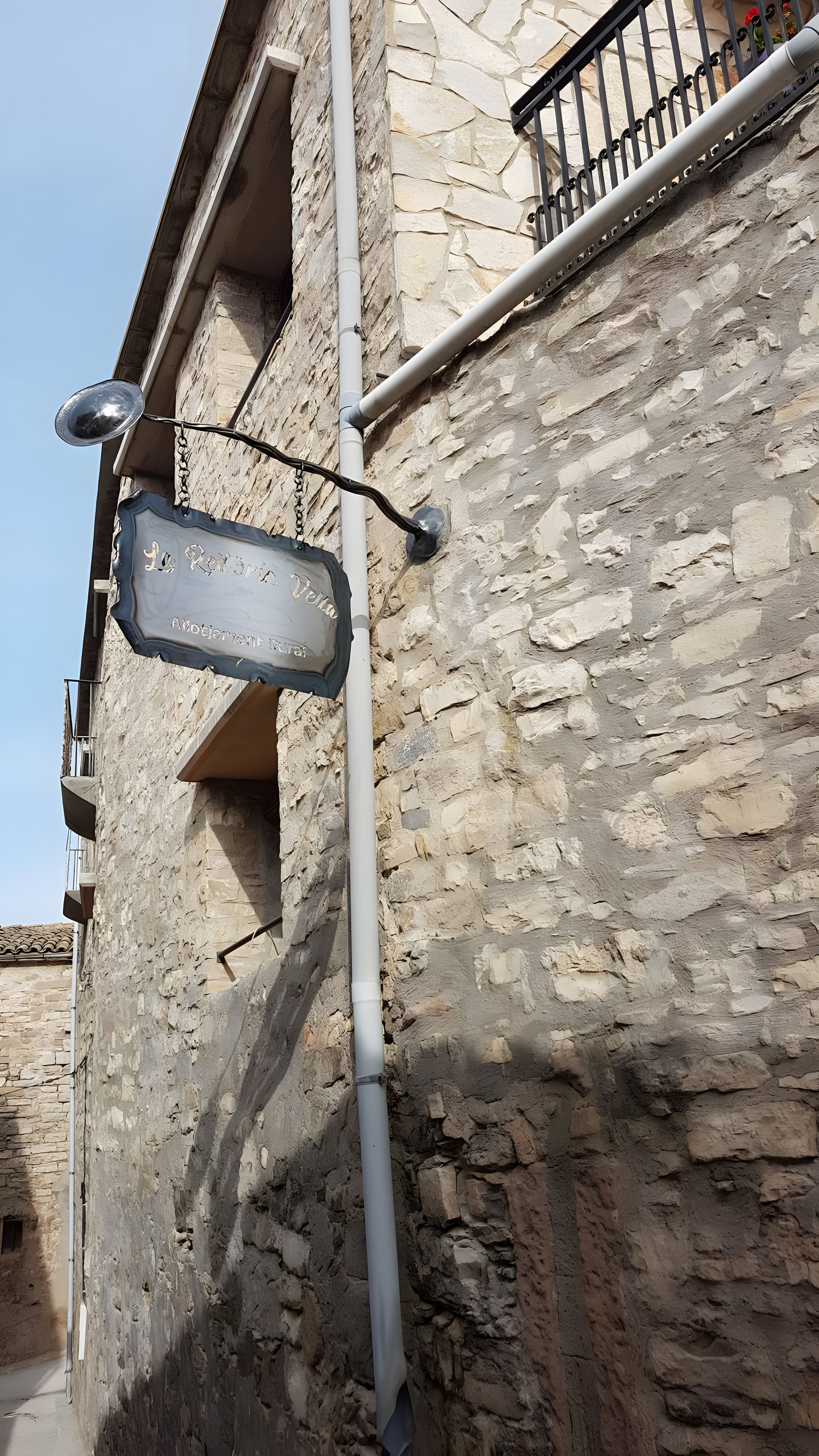 Un edificio de piedra con un letrero metálico colgado de un poste, una ventana y una barandilla de balcón.