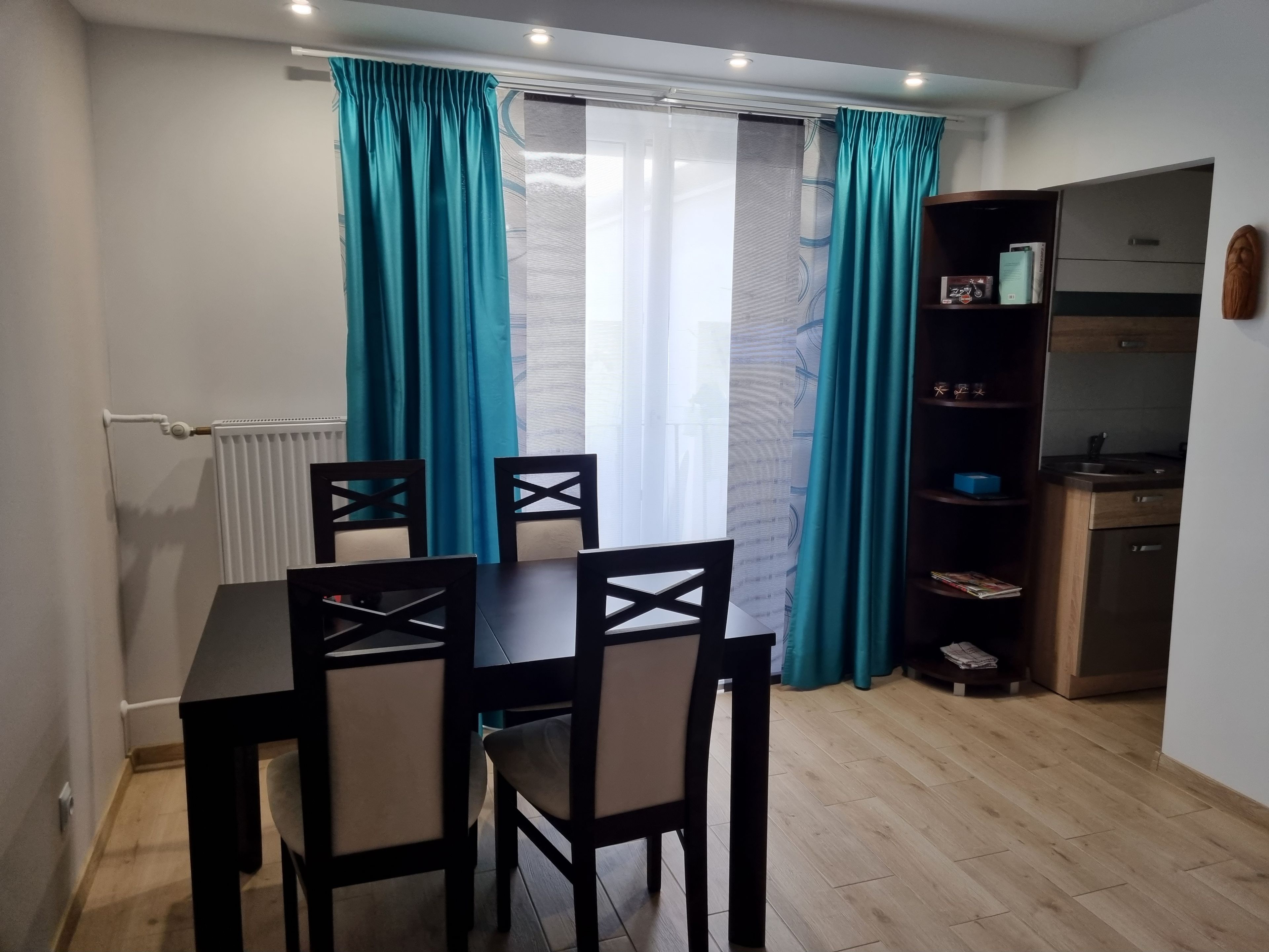 Un comedor con mesa y sillas, una cocina con armarios y electrodomésticos, y cortinas color turquesa.