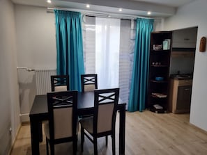 A dining area with a table and chairs, a kitchen with cabinets and appliances, and teal curtains.