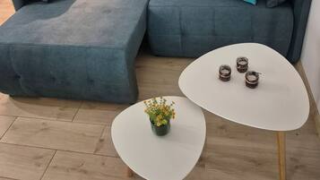 Una sala moderna con un sofá seccional, una pequeña mesa de centro blanca con una planta, y una mesa redonda blanca con tres vasos.