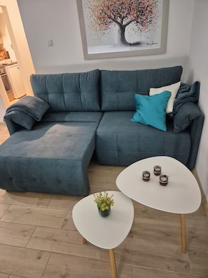 Ein modernes Wohnzimmer mit einer Eckcouch, einem kleinen weißen Couchtisch mit einer Pflanze und einem weißen runden Tisch mit drei Gläsern.