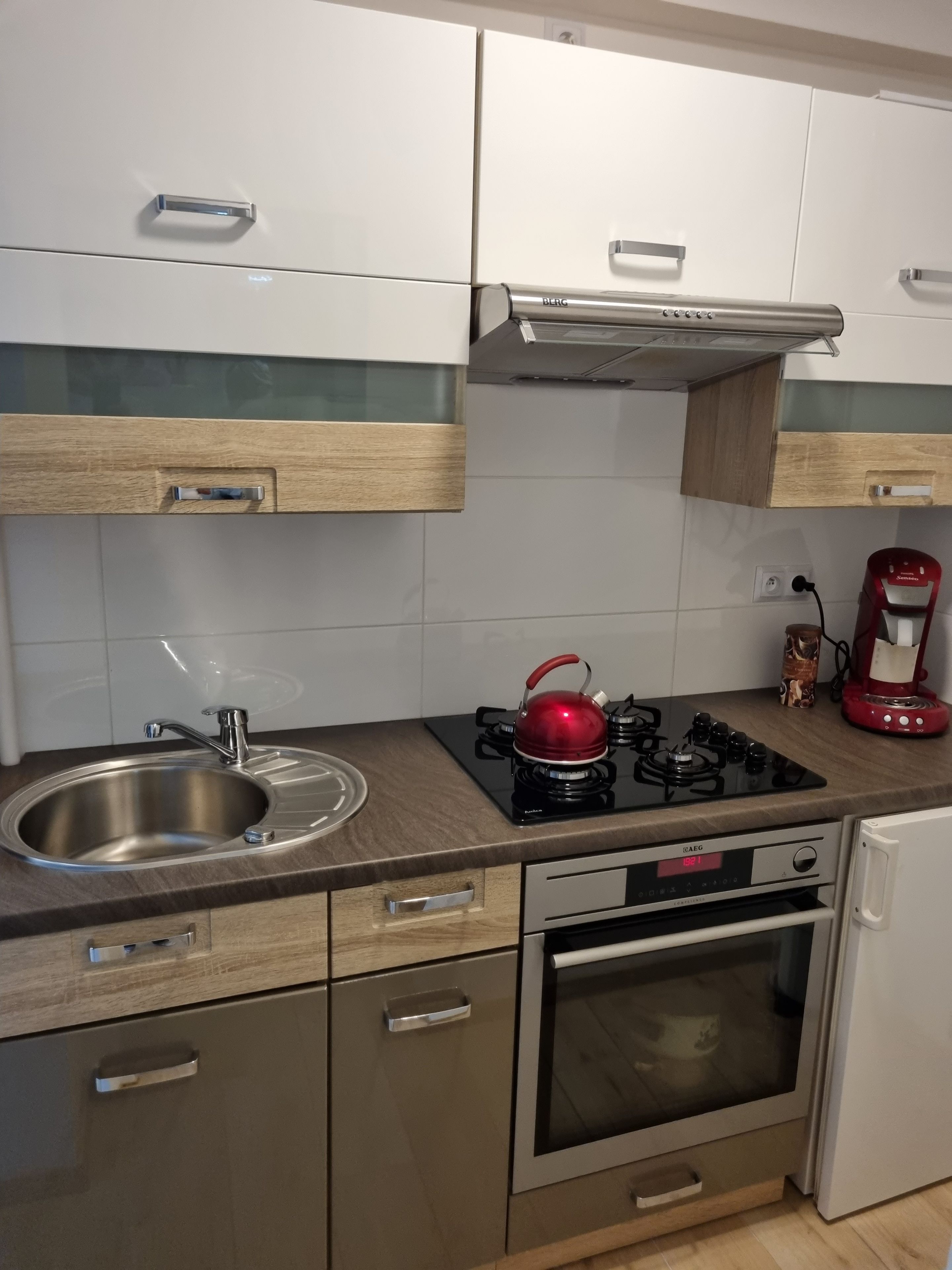 Una cocina moderna con electrodomésticos de acero inoxidable, una estufa a gas, una tetera roja y una cafetera.
