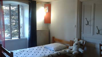 A bedroom with a bed, a window with curtains, a radiator, and a stuffed toy on the bed.