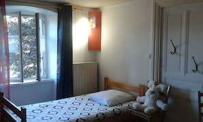 A bedroom with a bed, a window with curtains, a radiator, and a stuffed toy on the bed.