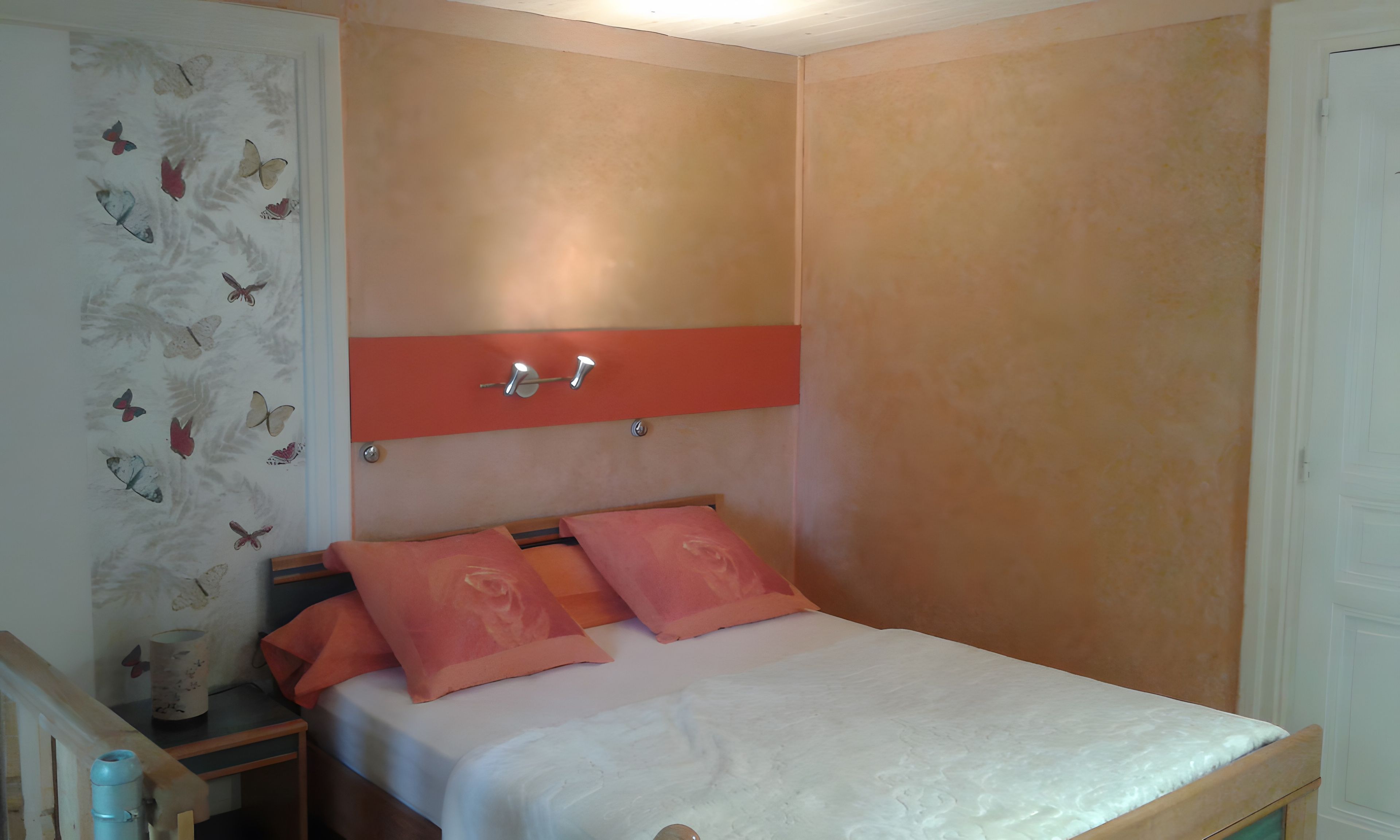 Une chambre à coucher comprenant un lit, une table de chevet, une étagère fixée au mur et des décorations murales représentant des papillons.