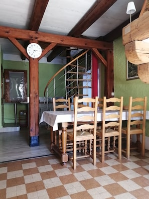A dining area with a wooden table and chairs, a clock on the wall, and a spiral staircase.