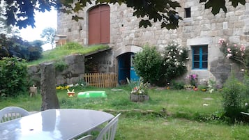A stone building with a wooden door and a window with blue shutters.