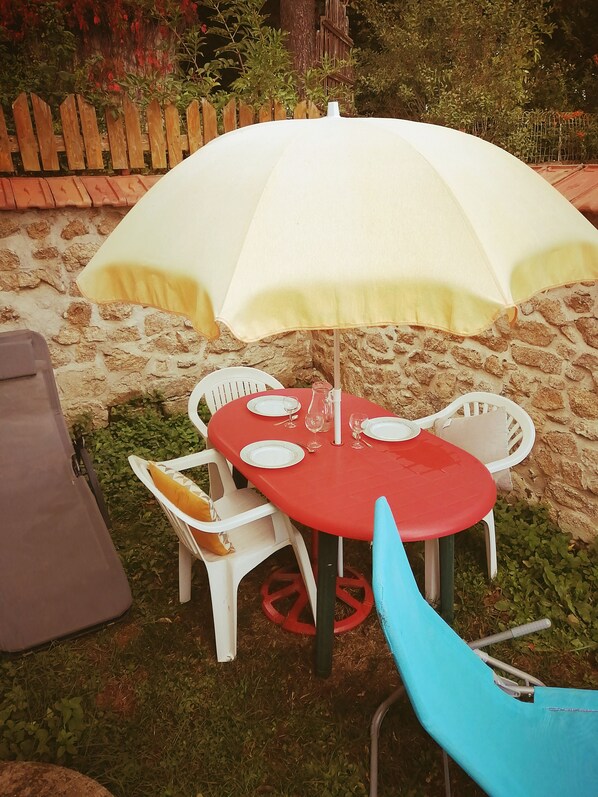 A red table with a white umbrella, white chairs, and a blue chair.