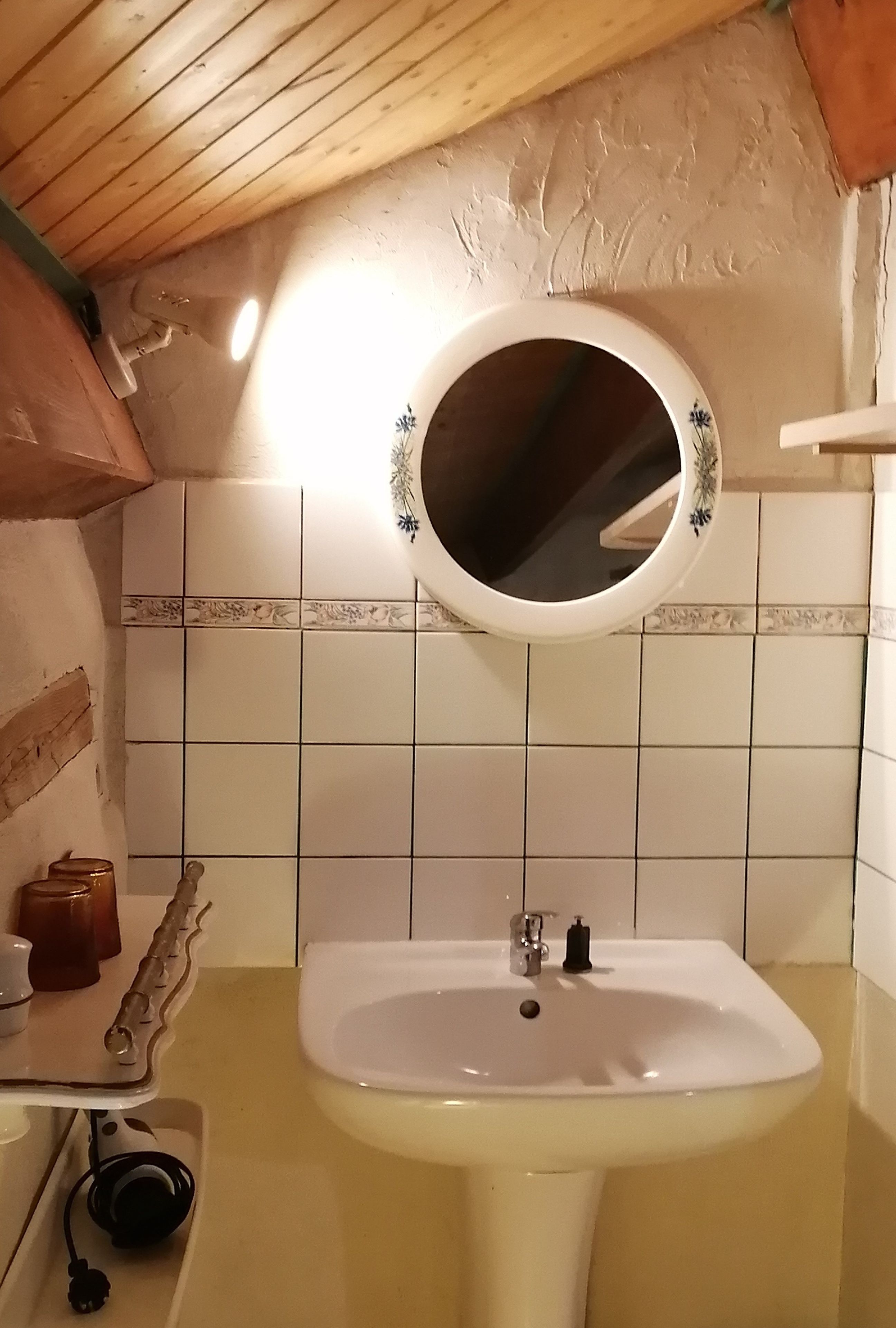 A bathroom with a white sink, a round mirror with a floral design, and a tiled wall.