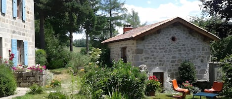 A stone house with a tiled roof, surrounded by a garden with various plants and flowers.