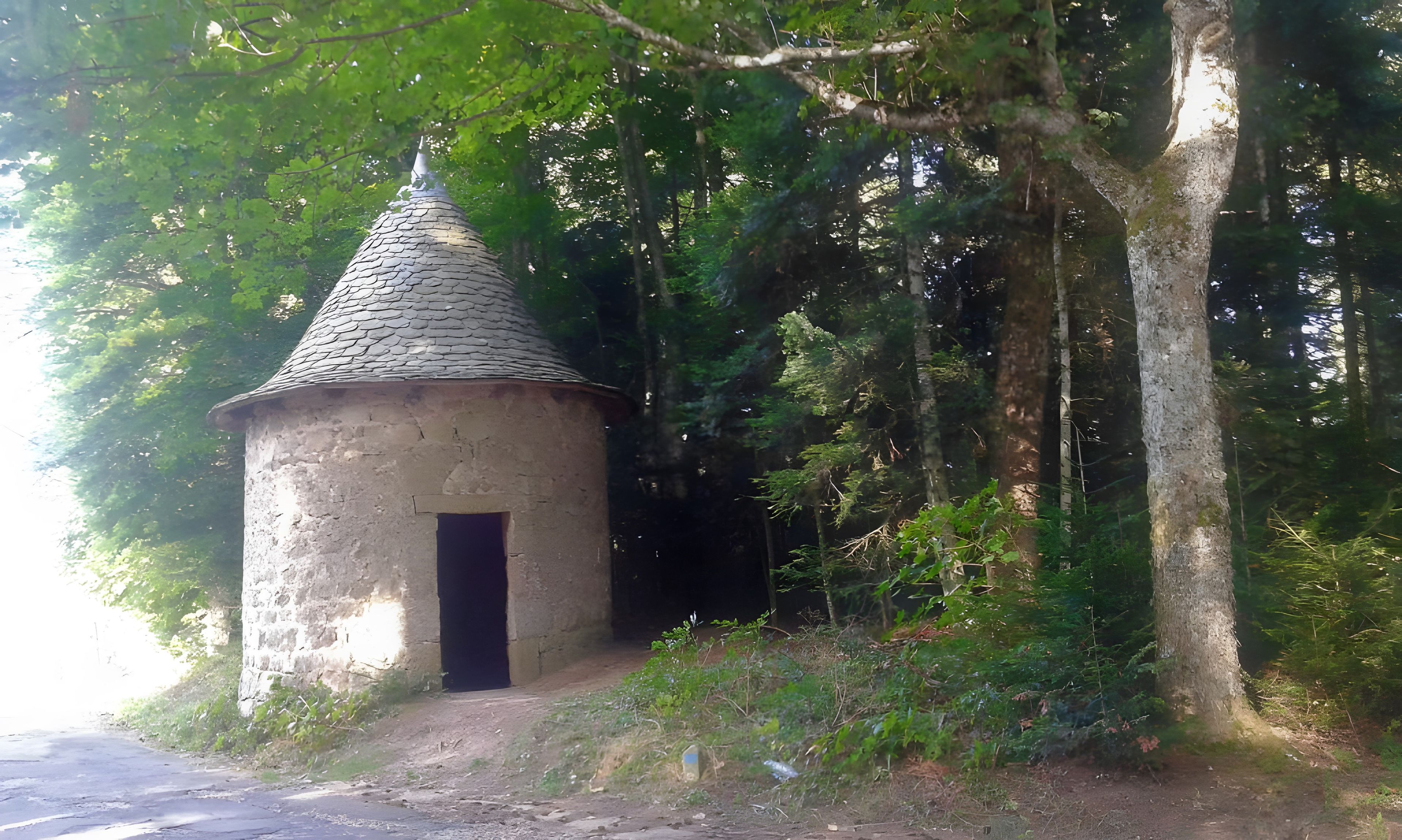 En lille stenhus med kegleformet tag, omgivet af tæt skov.