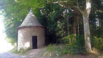 En lille stenhus med kegleformet tag, omgivet af tæt skov.