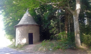 En lille stenhus med kegleformet tag, omgivet af tæt skov.