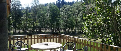 A patio with a round table and four chairs, surrounded by a wooden fence, overlooking a forested area.