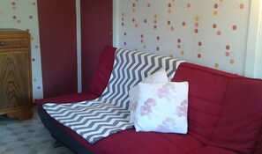 A red sofa with patterned cushions, a wooden cabinet, and a wall with circular decorations. - Cottage 'Le Petit Moulin' (Chenereilles)