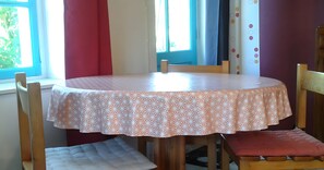 A round table with a patterned tablecloth, surrounded by wooden chairs with cushions. - Cottage 'Le Petit Moulin' (Chenereilles)