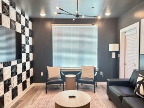 Ein modernes Wohnzimmer mit Wand in geometrischem Muster, einem runden Couchtisch, zwei Sesseln, einem Sofa und einer Deckenleuchte.